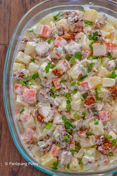 a glass bowl filled with potato salad on top of a wooden table next to a knife