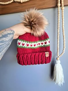 a hand holding a red hat with a pom - pom on it