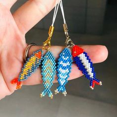 a hand holding three small cross stitch fish key chains