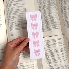 a bookmark with pink bows is held in front of an open book that has pages spread out