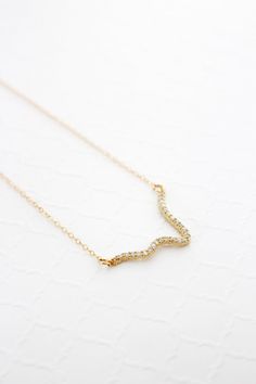 a gold necklace with diamonds hanging from it's sides on a white surface,