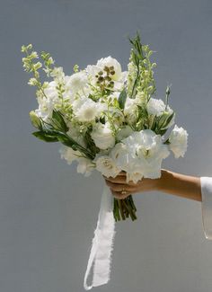 a bouquet of white flowers being held by a person's hand in front of a gray background