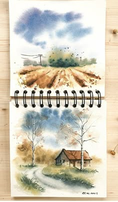 two notebooks with watercolor drawings on them, one has a farm scene and the other is a country road