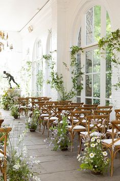 a room filled with lots of wooden chairs covered in plants and flowers next to windows