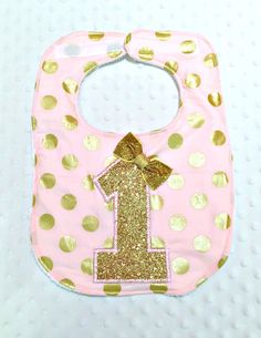 a pink bib with gold polka dots and a number one on the front,