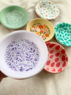 five colorful bowls sitting on top of a white cloth covered table next to each other