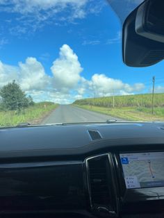 the dashboard of a car driving down a country road with blue skies and clouds in the background