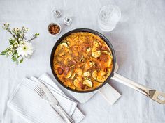 a skillet filled with food sitting on top of a white table cloth next to silverware