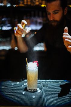 the bartender is making a drink at the bar with his hand on the glass and another man in the background