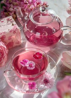 a tea pot filled with pink liquid next to a box and flowers on a table