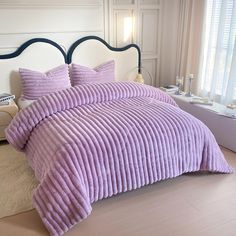 a bed with purple bedspread and pillows in a bedroom next to a window