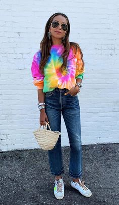 a woman standing in front of a white brick wall wearing sunglasses and a tie dye shirt