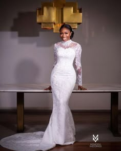 a woman standing in front of a table wearing a white wedding dress with long sleeves