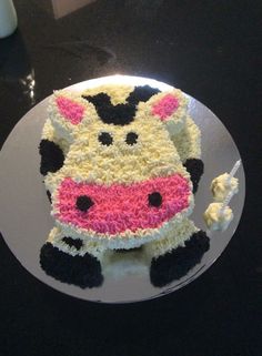 a cake that is shaped like a cow on a white plate with black and pink icing