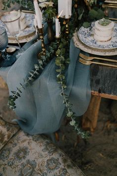 the table is set with blue and white plates, silverware, candles and greenery