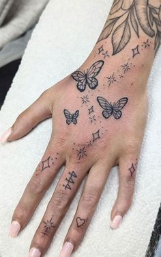 a woman's hand with tattoos on it and butterflies in the sky above her