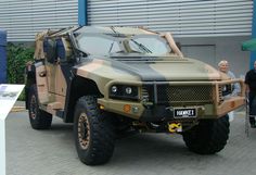 an army vehicle parked in front of a building with people looking at it and two men standing next to it