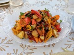 a white plate topped with vegetables on top of a table next to glasses and utensils