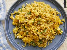 a blue plate topped with noodles and vegetables on top of a white table cloth next to a fork