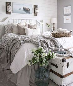 a white bed topped with lots of pillows and blankets next to a vase filled with flowers