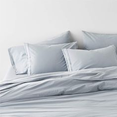 an unmade bed with light blue sheets and pillows