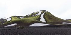 the mountain is covered in snow and green mossy grass with white patches on it