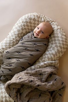 a baby wrapped in a blanket laying on top of a bed next to a wall