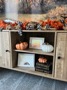 a wooden cabinet with pumpkins and other decorations on the top shelf in front of a painting