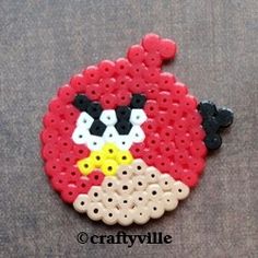 a red and black beaded angry bird brooch on a gray surface with white dots