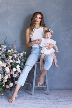 a woman sitting on a stool holding a baby and posing for a photo with flowers in the background