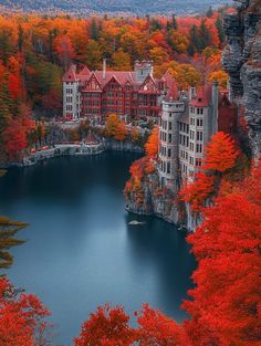 a lake surrounded by trees with red leaves in the foreground and buildings on the other side