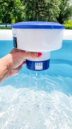 a hand holding a blue and white water container over the top of a swimming pool