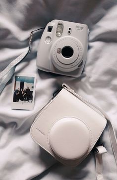 a white camera sitting on top of a bed next to a small card and bag