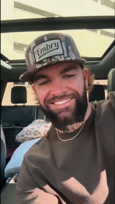 a man with a beard wearing a hat in the back seat of a car smiling