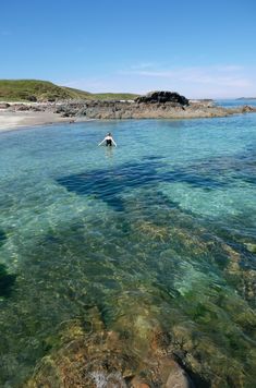 a person swimming in clear blue water near the shore