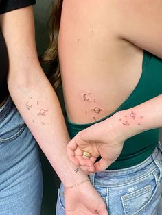 two women holding hands with tattoos on their stomachs and the other arm behind them