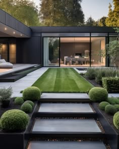 an outdoor area with steps, grass and bushes in front of a modern house at dusk