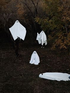 three white cloths are hanging from trees in the woods, with ghost like decorations on them