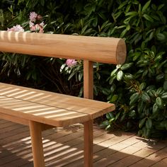 a wooden bench sitting on top of a brick floor next to green bushes and flowers