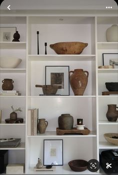 shelves with vases, bowls and other items on them in a room that has white walls