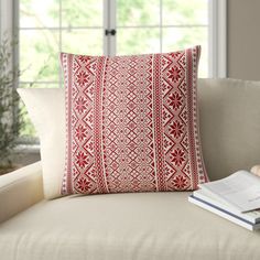 a red and white pillow sitting on top of a couch next to a book near a window