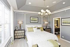 a bedroom with gray walls and white bedding, chandelier, windows, and pictures on the wall