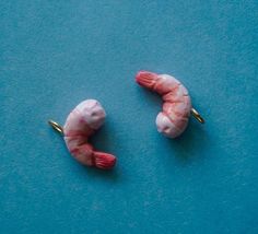 two pink shrimp on a blue surface with some gold pins sticking out of it's sides