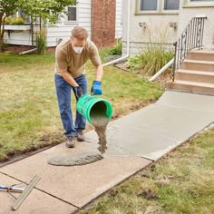 a man is pouring cement into a bucket on the sidewalk in front of a house