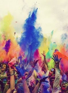 people are throwing colored powder in the air at an outdoor event with their hands up