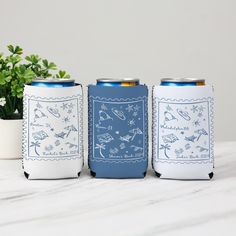 three can coolers sitting next to each other on a white table with a plant in the background