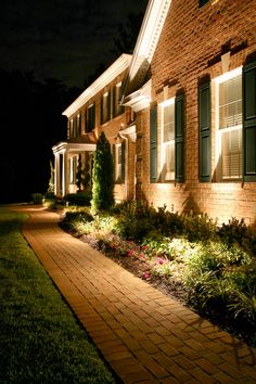 a house that is lit up at night with the lights on and flowers in the front yard