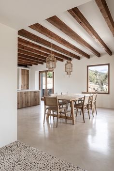 a dining room table and chairs in front of an open window with wooden beams on the ceiling