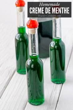 three green bottles with red caps sitting next to each other on a white wooden table