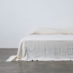 an unmade bed with white linens on the top and bottom, against a plain wall